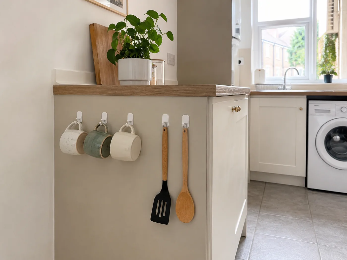 Adhesive hooks on kitchen wall holding mugs and cooking utensils
