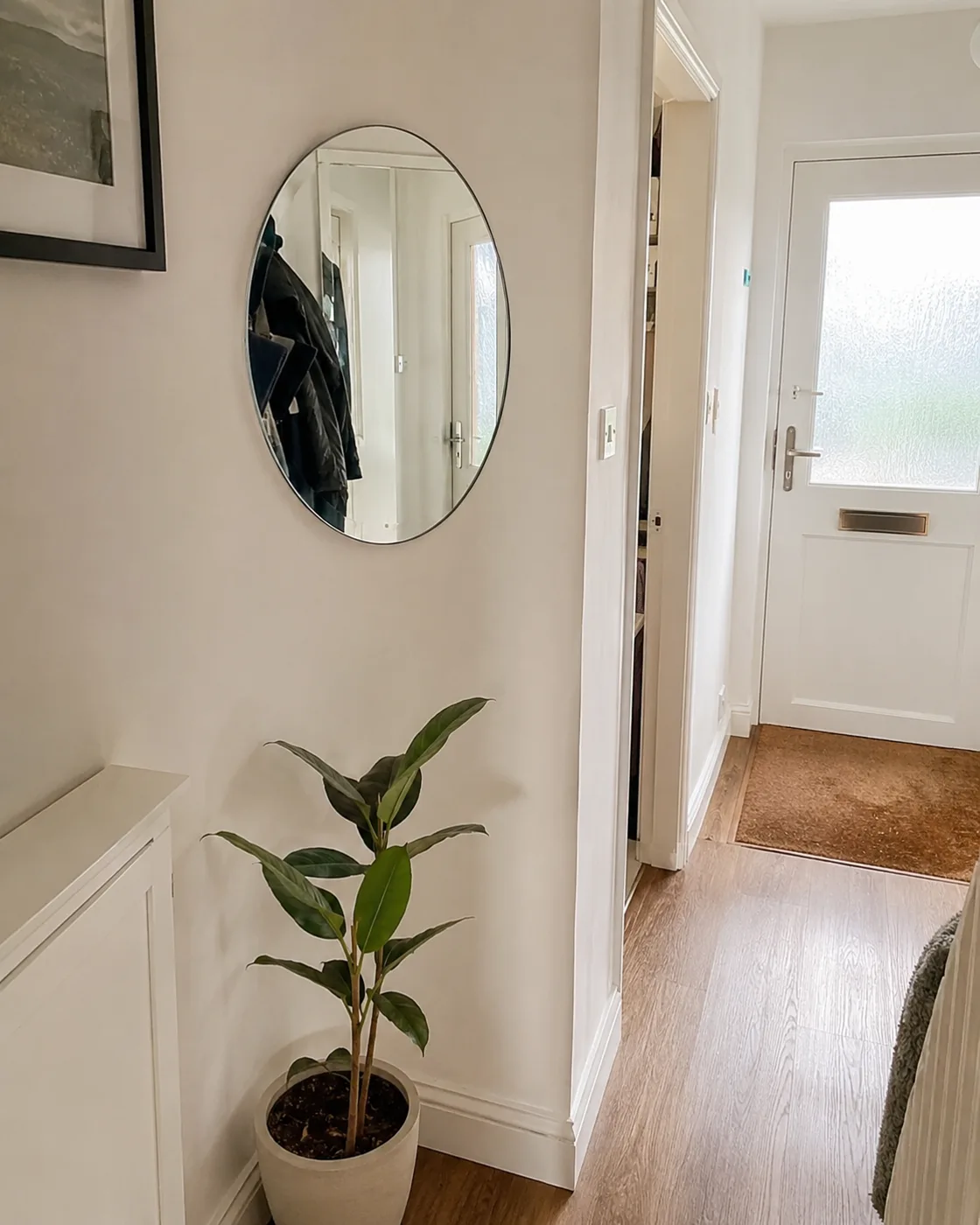 Small round mirror on hallway wall using adhesive strips with plant below
